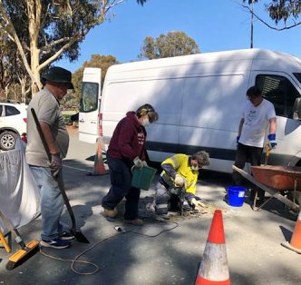 The image shows a group of people working on a roadside construction site, with a van and a red cone marking the area.
AI-generated content may be incorrect.