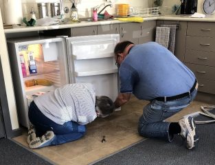 A person and person looking at a small refrigerator

Description automatically generated