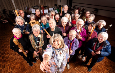 The image depicts a group of elderly people gathered in a room, holding various musical instruments and standing in a circle.

AI-generated content may be incorrect.