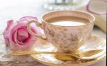 A delicate porcelain cup with a floral pattern is filled with cream, accompanied by a pink rose and gold spoon.

AI-generated content may be incorrect.